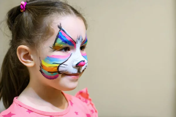 Kid with face painting of kitty, cute little girl with painted mask on face of rainbow cat. Portrait of pretty child with beautiful makeup and copy space background, unique facial body art for party.