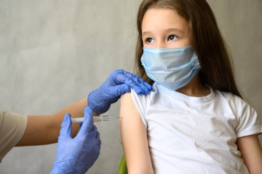 Vaccination of kid from COVID-19 or flu, cute little girl in mask during coronavirus vaccine injection. Doctor vaccinates adorable child. Concept of immunization, corona virus, shot and health. clipart