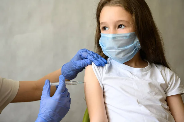 Vaccination of kid from COVID-19 or flu, cute little girl in mask during coronavirus vaccine injection. Doctor vaccinates adorable child. Concept of immunization, corona virus, shot and health.