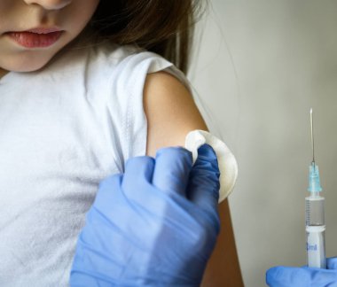 Klinikte çocuk iğnesi, COVID-19 Corona virüsü ya da grip aşısı sırasında küçük tatlı bir kız çocuğu, doktorların ellerine bakan sevimli bir çocuk. Bağışıklık, sağlık ve koronavirüs aşısı kavramı.