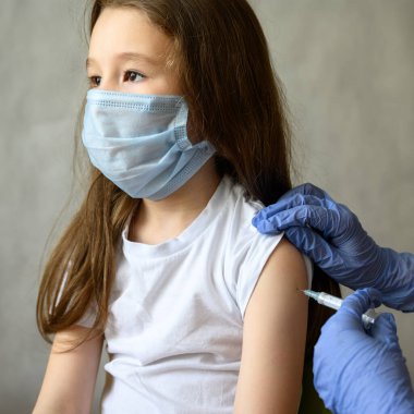 COVID-19 ya da grip aşısı ya da Coronavirus aşısı sırasında küçük tatlı bir kız. Maskeli ve şırıngalı sevimli bir çocuğun portresi. Corona virüsü, aşılama ve aşı kavramı