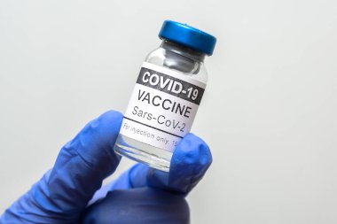 Beyaz arka planda COVID-19 aşı şişesi, doktor eldiveni kapağında koronavirüs aşısı şişesi. Corona virüsü salgını sırasında ilaç, aşı, aşı, aşı kavramı.