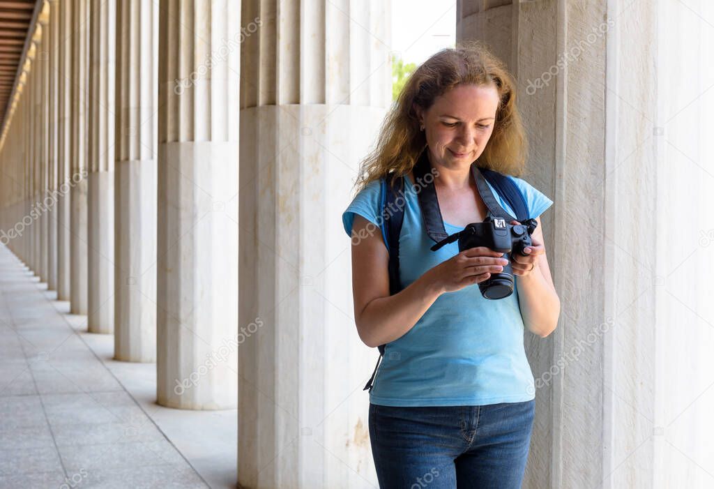 Female tourist in Stoa of Attalos, Athens, Greece, Europe. Young woman plays images in camera at Ancient Greek columns. This place is landmark of Athens. Concept of travel and photography in Athens.