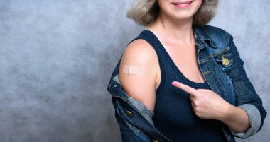 COVID-19 aşısı olduktan sonra kolunu sıva ile gösteren bir kadın. Coronavirus aşılanmış sağlıklı bir insan gri arka planda omuz gösteriyor. İnsanlar aşı, iğne, iğne ve korona virüsü konsepti. 