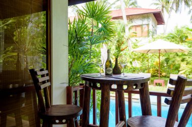 Şarap şişesi ve bardaklarla servis edilen masa. Villada ya da evin dışında. Tropik otellerde palmiye ağaçları ve havuzu olan bir bahçe. Teraslı bir avlu, yazlık yazlık evlerin arka bahçesi..