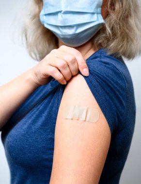 Aşılanmış genç bir kadın koluna alçı takmış. COVID-19 aşısından sonra maske takmış bir kadın. Korona virüsü aşısı, enjeksiyon, aşı ve koronavirüs aşısı kavramı.