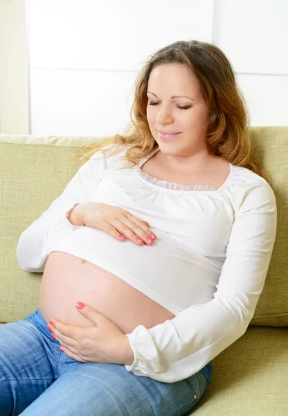 Szczęśliwy w ciąży kobieta siedzi na kanapie w domu — Zdjęcie stockowe