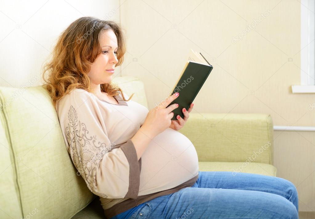 Cute pregnant woman reading a book at home