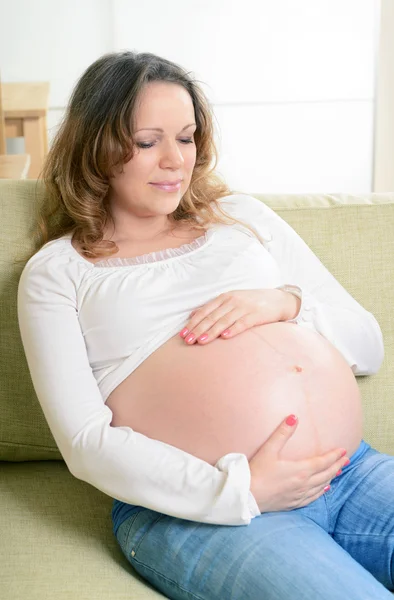 Mujer embarazada feliz sentada en el sofá en casa —  Fotos de Stock