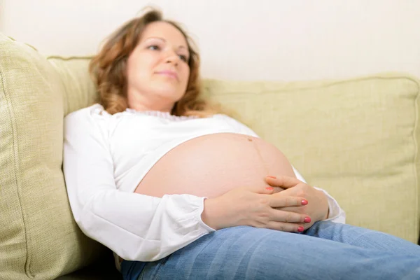 Nadenkend zwangere vrouw zittend op de Bank thuis — Stockfoto