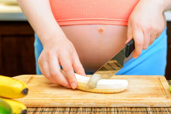 Pregnant woman prepares a banana in the kitchen — Stock Photo, Image