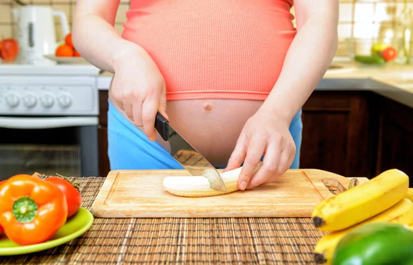 Kobieta w ciąży przygotowuje banana w kuchni — Zdjęcie stockowe