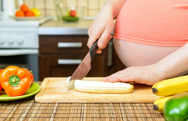 Zwangere vrouw bereidt een banaan in de keuken — Stockfoto