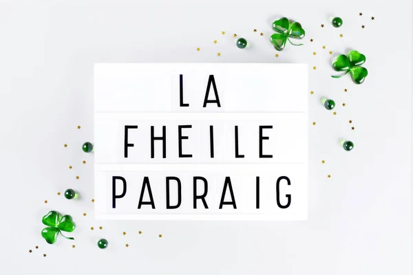 Lightbox with Saint Patricks day text written in irish and green glass shamrocks — Stock Photo, Image