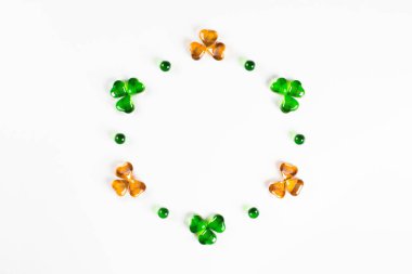 Yeşil ve turuncu cam kalplerden oluşan yuvarlak çerçeve beyaz arka planda yoncalar 