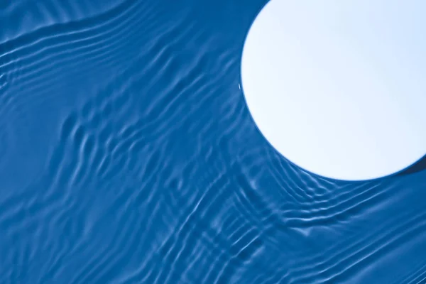 透明な濃い青の水の背景に空の白い円の表彰台 — ストック写真