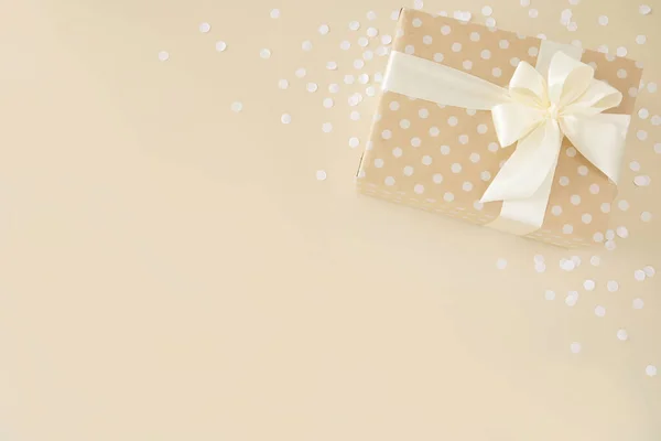 Regalo beige avvolto in carta punteggiata con fiocco bianco su sfondo beige — Foto Stock