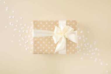 Bej arka planda beyaz fiyonklu noktalı kağıda sarılmış bej rengi hediye.
