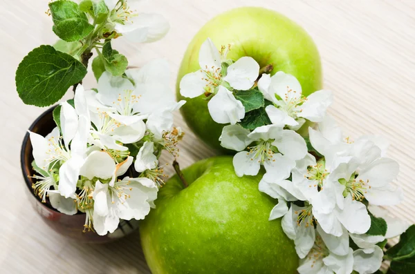 Grönt äpple med en gren av en blommande äppelträd — Stockfoto