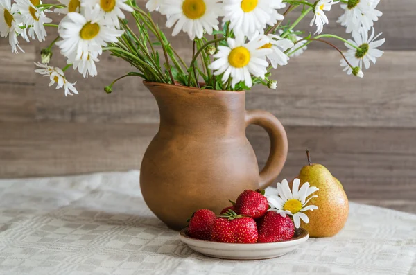 Strauß Gänseblümchen im Tonkrug und Erdbeeren mit Birnen. — Stockfoto