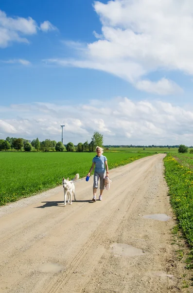 Mulher com um cão vai em uma estrada de campo — Fotografia de Stock