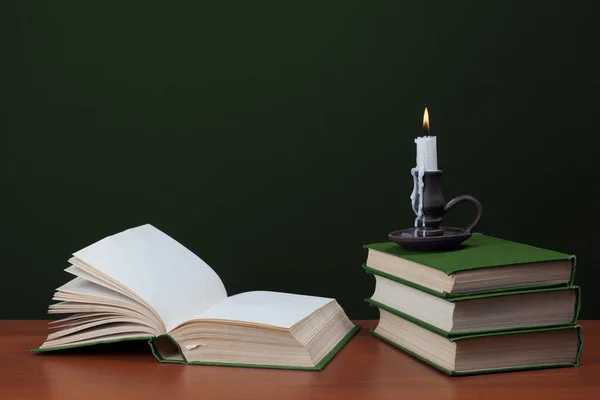 Open blank book and stack of books with burning candles on green background — Stock Photo, Image