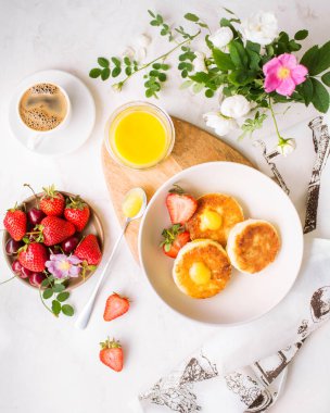Taze dutlu yaz kahvaltısı. Mango soslu ve çilekli peynirli kek. Beyaz arka planda taze demlenmiş espresso kahvesi. Güzel kahvaltı servisi. Çiçekli yemek servisi.
