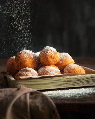 Kahverengi ahşap bir masada, keten peçetenin yanında süzme peynirli çörekler. Pudra şekeri tatlı olarak koyulur.