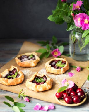 Ahşap bir masada kirazlı küçük bisküviler pişirdim. Böğürtlenli yaz kekleri ve kır tarzında pembe çiçekler.