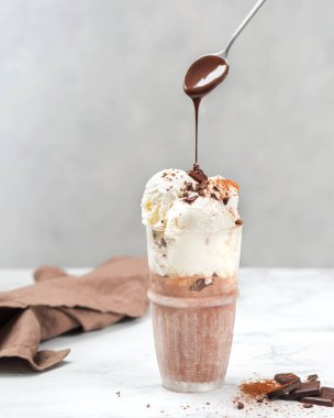 Vanilyalı ve çikolatalı dondurma. Çikolata parçacıklı. Hafif bir arka planda kaşıkla tatlı.