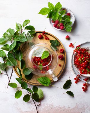 Hafif arka planda sıcak bir içecek. Ahududu ve kırmızı üzümlü çilek çayı. Çaydanlıkta böğürtlenlerden yapılan çay. Yaz, yapraklar ve çayla dolu bir hayattır. Taze ahududu hasadı