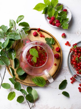 Hafif arka planda sıcak bir içecek. Ahududu ve kırmızı üzümlü çilek çayı. Çaydanlıkta böğürtlenlerden yapılan çay. Yaz, yapraklar ve çayla dolu bir hayattır. Taze ahududu hasadı