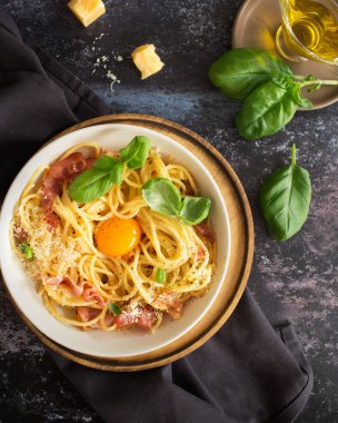 İtalyan mutfağı. Pastırmalı ve yumurtalı makarna. Parmesan peynirli ve fesleğenli spagetti. İtalyan yemeği. Karanlık arka planda İtalyan yemekleri. Zeytinyağı