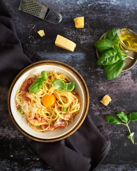 Italian cuisine. Pasta carbonara with bacon and egg. Spaghetti with parmesan cheese and basil. Italian dinner. Italian food on a dark background. Olive oil