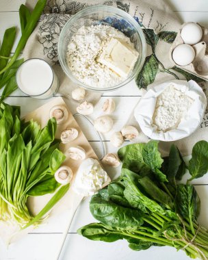French cuisine. Prepare quiche with mushrooms, spinach and wild leeks. Green food. Baking products on a white table. Pie with cheese and mushrooms. Flour, butter, eggs and cream, wild garlic. clipart