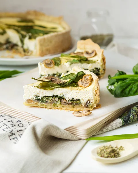 French cuisine. Quiche with mushrooms, spinach and wild leeks. Green food. French pastries on a white table. Pie with cheese and mushrooms, wild garlic. French dish with spinach, wild garlic.