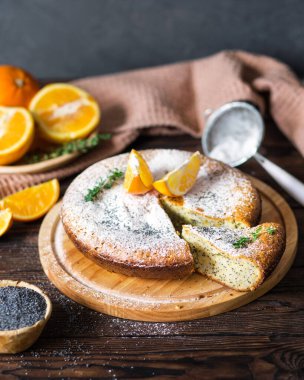 Meyveli hamur işleri. Haşhaş tohumlu turuncu pasta. Bir dilim pasta. Ahşap kahverengi arka planda portakallar. Yemek fotoğraflarında metin için bir yer.