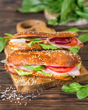 Lezzetli bir yemek. Domatesli sandviç, ıspanak ve jambonlu. Ahşap bir arka planda Aperatif. Susamlı çörek. Amerikan mutfağı. Taze yemek..