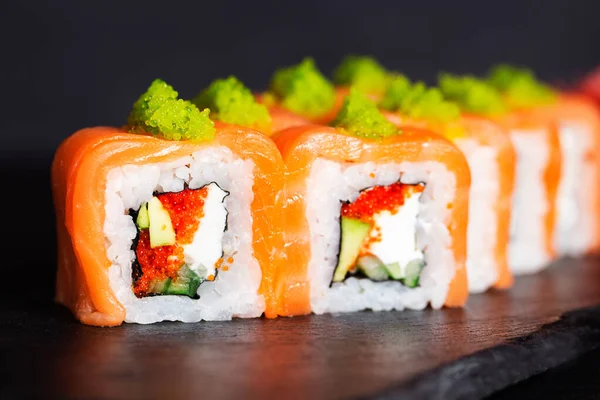 Japanese cuisine. Salmon rolls with avocado. Japanese food on a black background. Green caviar of flying fish. Tobiko. Macro photography of sushi. Close-up of the rolls