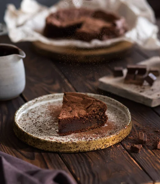 Chocolate cake on a wooden table. A piece of brownie on a brown background. Cocoa and chocolate pieces. Serving dessert.