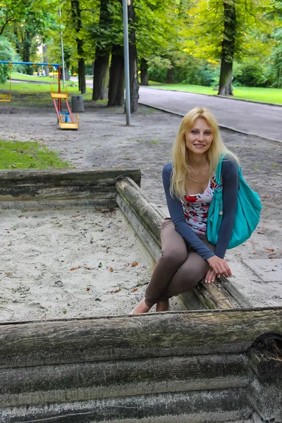 Mujer joven sentada en el parque infantil en el parque de la ciudad —  Fotos de Stock