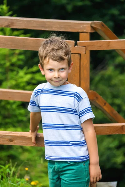 Leende pojke står nära den ett trästaket — Stockfoto