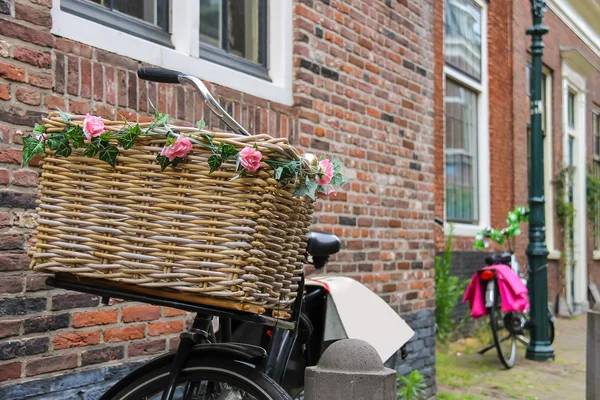 Cykel med blomst dekoreret fletkurv nær mursten hus - Stock-foto