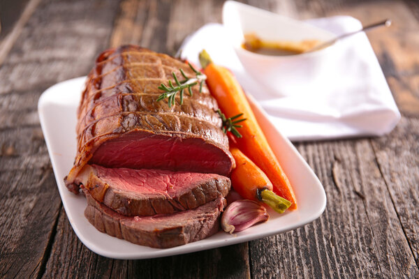 Roast meat on board with carrot and herb served on wooden table
