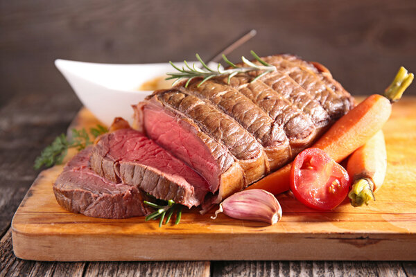 Roasted beef fillet on wooden board with vegetables and rosemary, close up