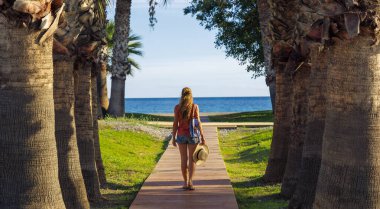 Kadın palmiye ve hindistan cevizi boyunca yürüyordu. Denize doğru gidiyordu. Yaz gezisi, dinlendirici tatil