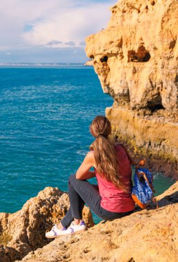 Altın kayalıklarda oturan kadın Atlantik Okyanusu 'nun tadını çıkarıyor, Portekiz' de Algarve