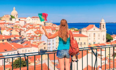 Elinde Portekiz bayrağı olan bir kadın güneşli bir günde Portekiz, Lizbon şehrinin kendine özgü kırmızı çatılarına hayran.