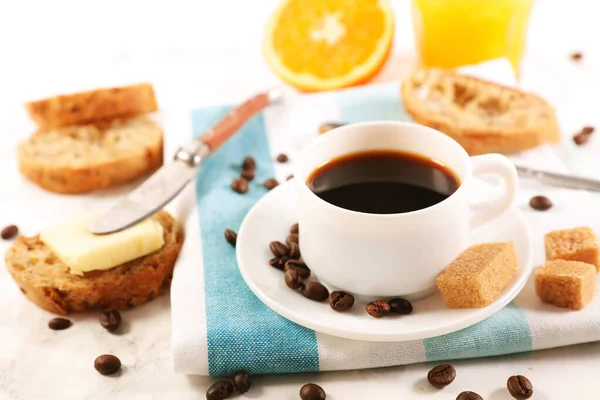 Bir fincan kahve, esmer şeker ve kahve çekirdeği ile portakal suyu ve tereyağlı ekmek.