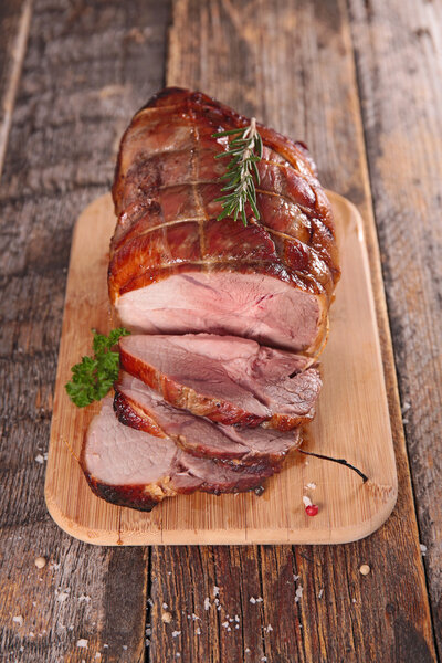 Sliced roasted pork meat on board on wooden table